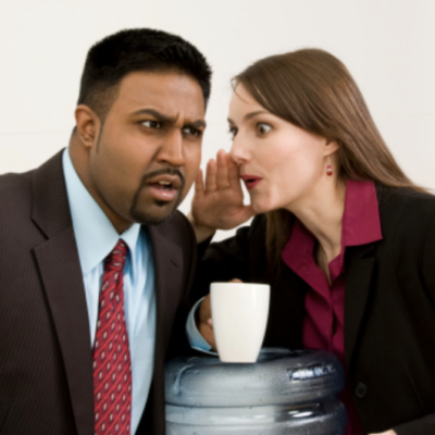 a women in business atire whispering to her male coworker at the water cooler.